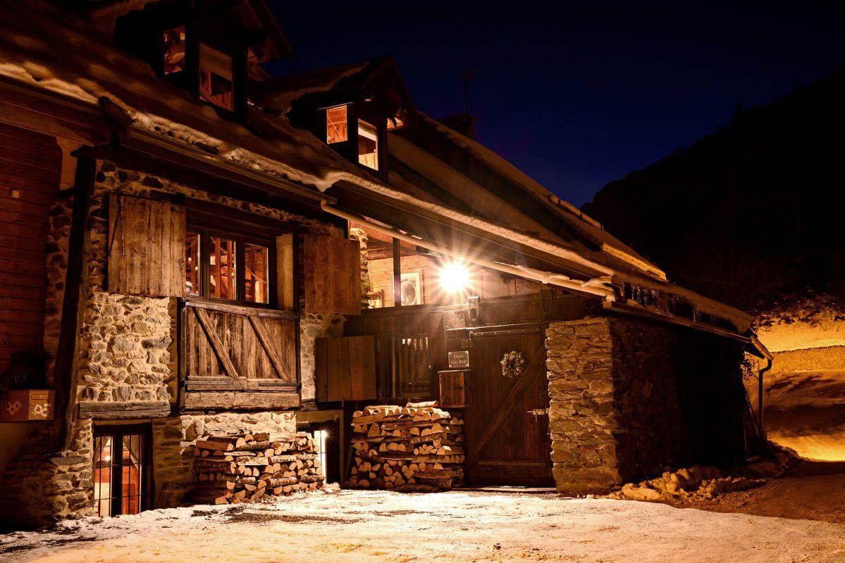 Chalet exterior at night with stacked firewood for the wood-burning fireplace
