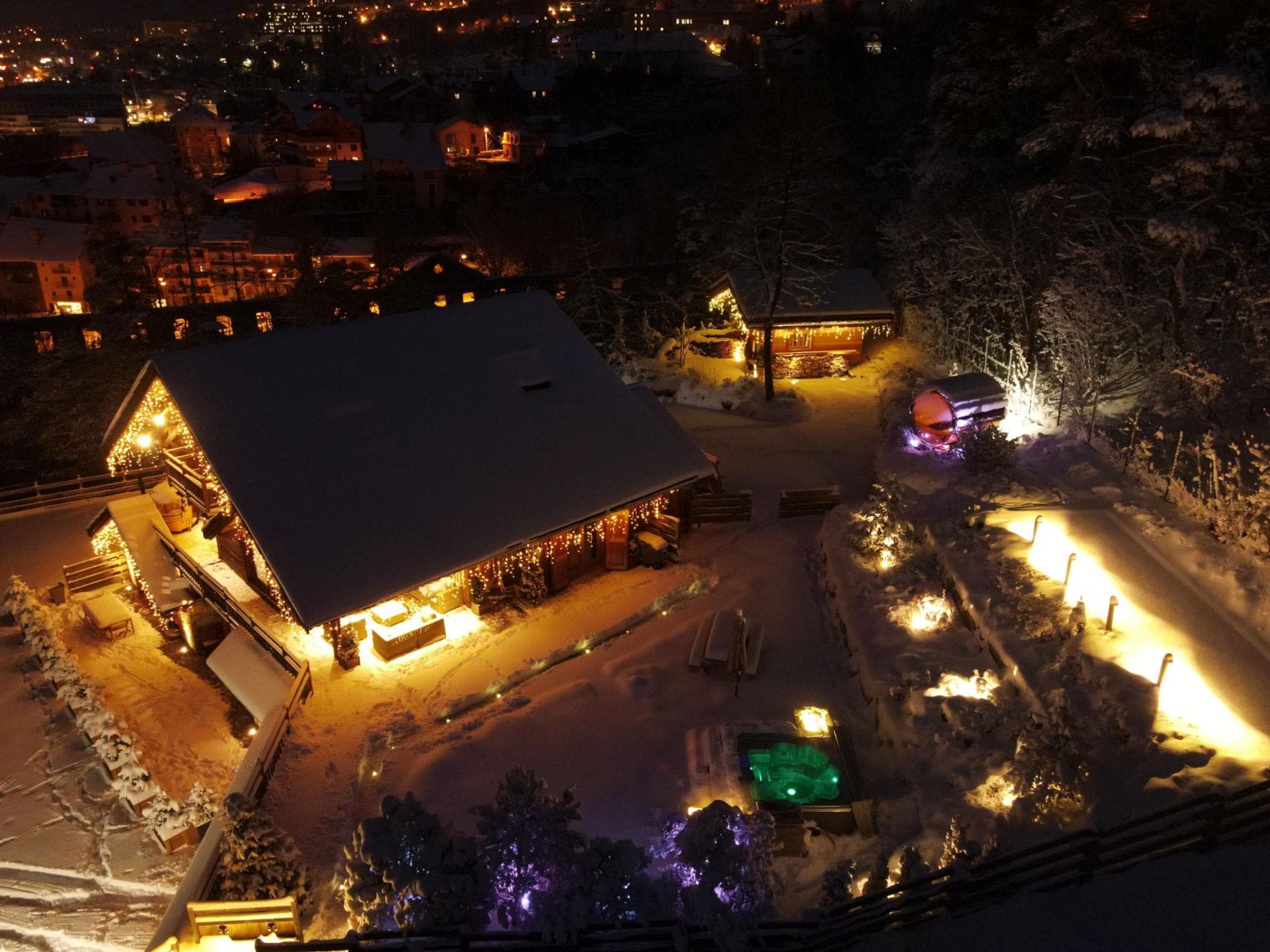 Aerial night view of chalet with outdoor hot tub and barrel sauna