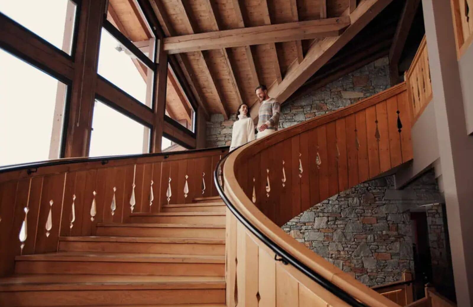 Curved wooden staircase with stone accent wall and vaulted timber ceilings
