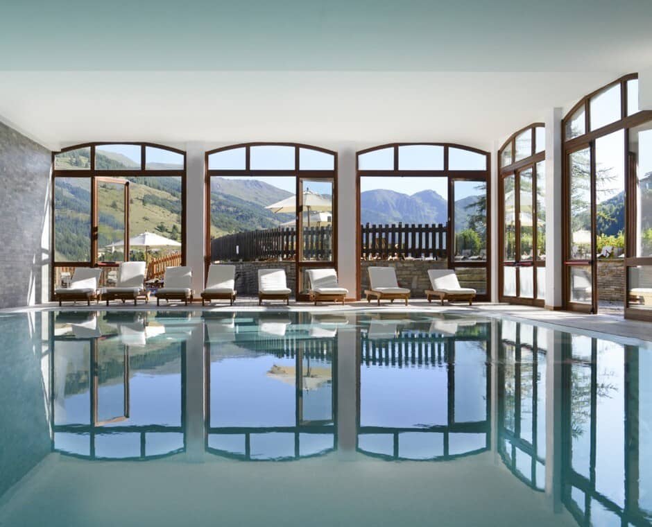 Indoor heated pool with mountain views and poolside lounge seating