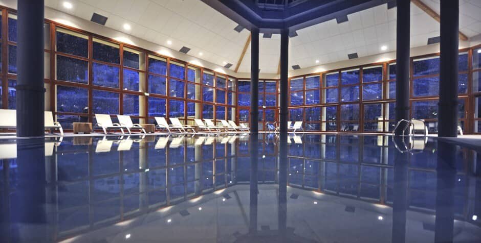 Indoor pool with floor-to-ceiling windows and poolside lounge seating