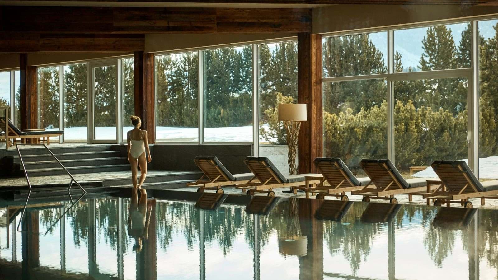 Indoor heated pool with poolside loungers and floor-to-ceiling forest views
