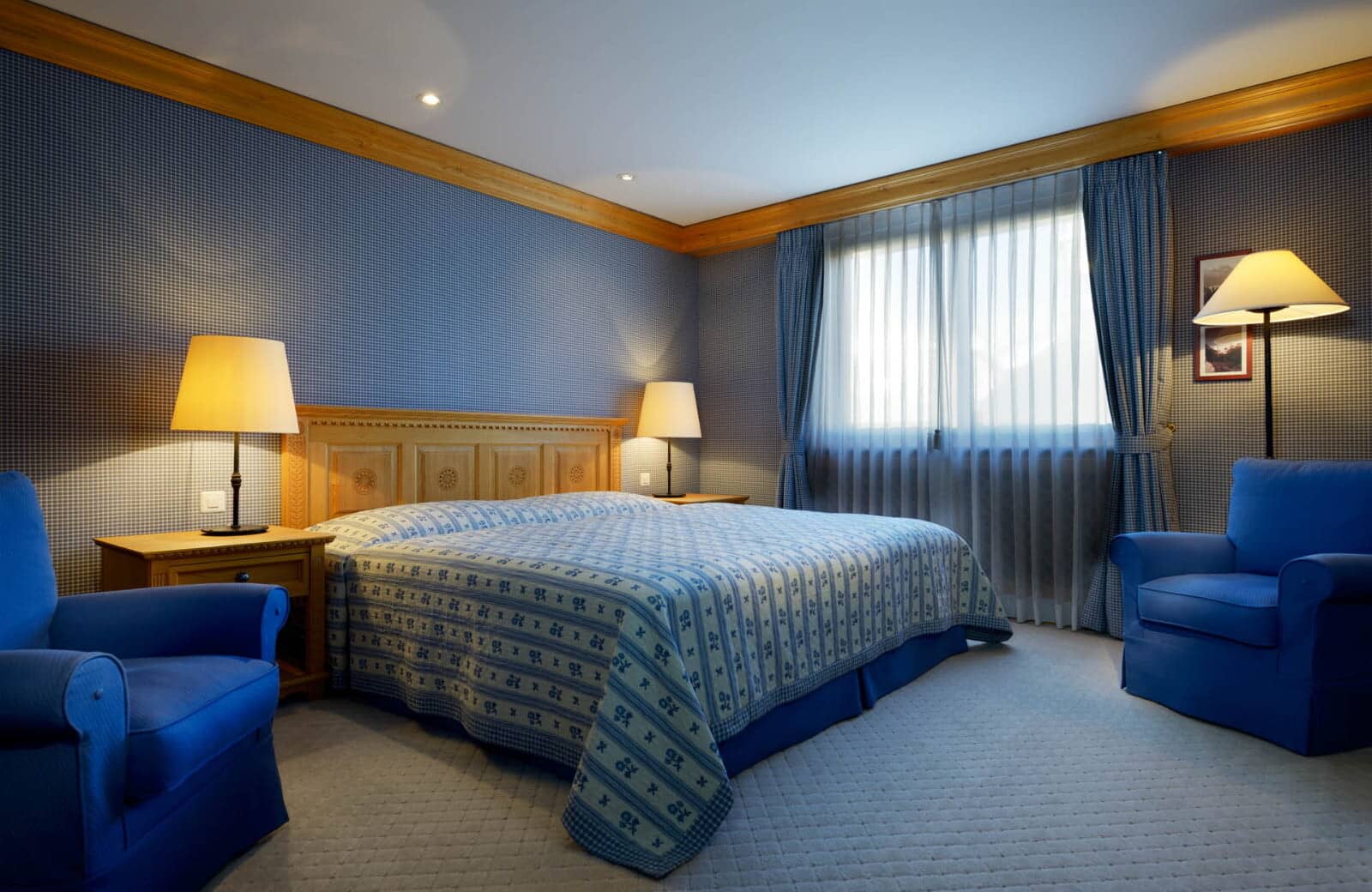 Primary bedroom with king bed, wood headboard, dual nightstands with lamps, and layered curtains with sheer panels