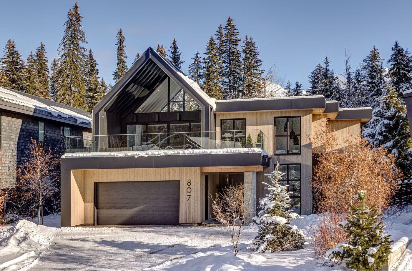 Chalet exterior featuring heated driveway and two-car garage with glass-railing balcony