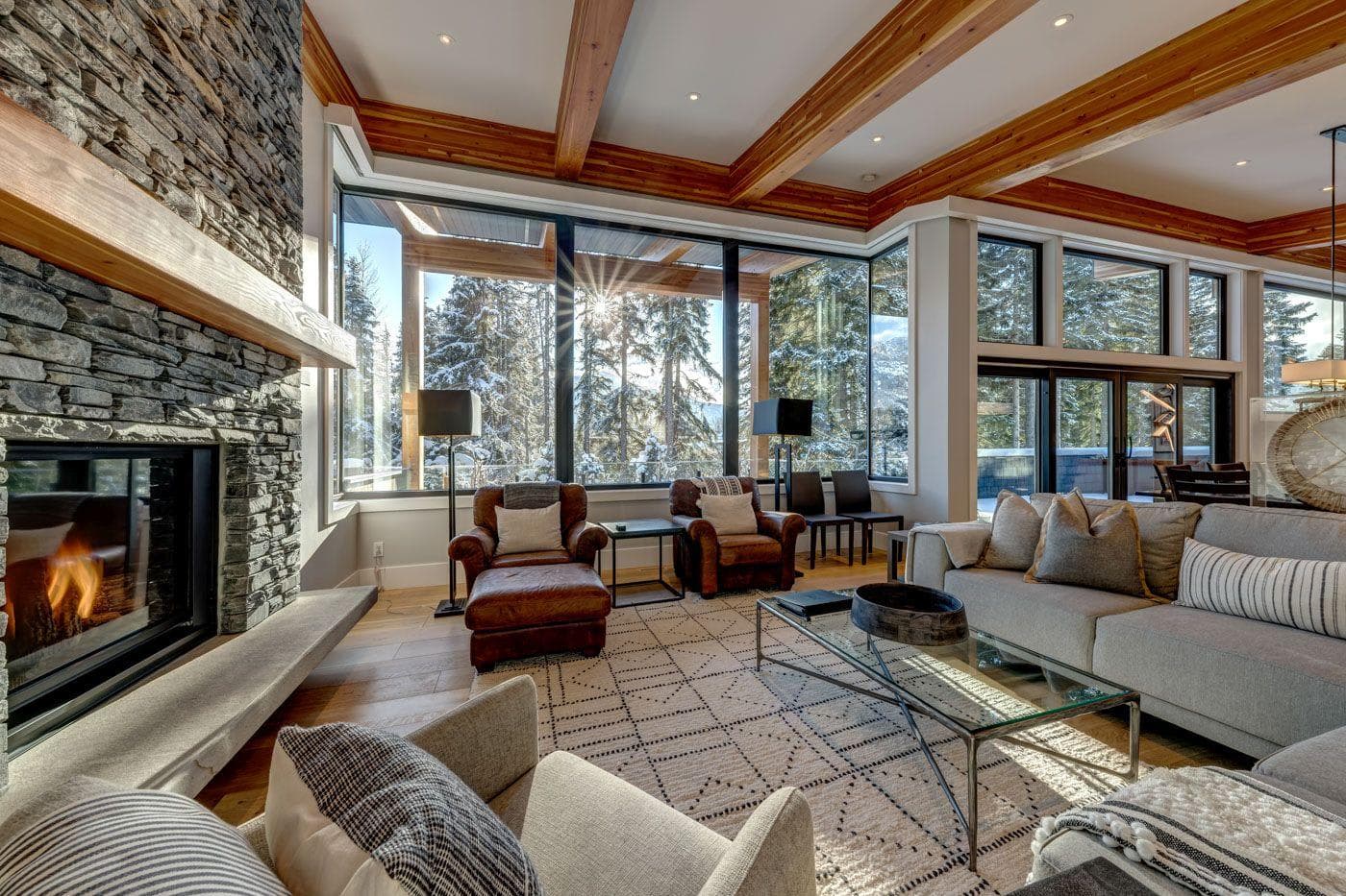 Living room with stone fireplace and floor-to-ceiling forest views