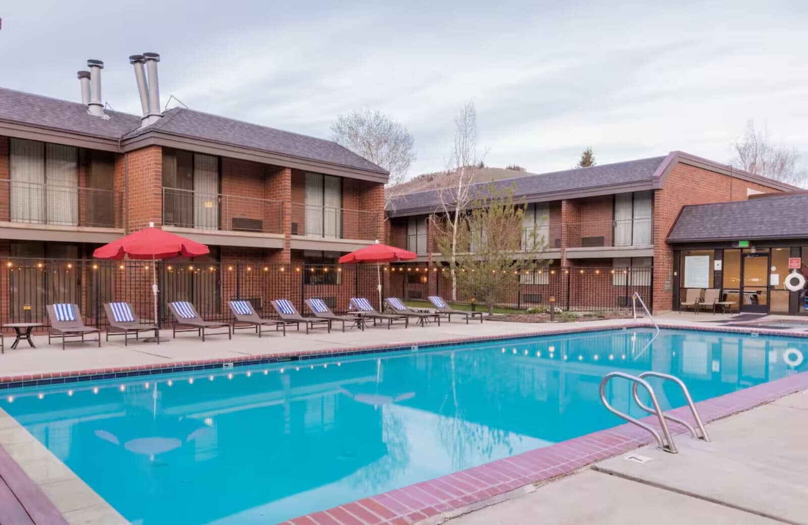 Shared outdoor pool with lounge seating and fence-mounted string lighting