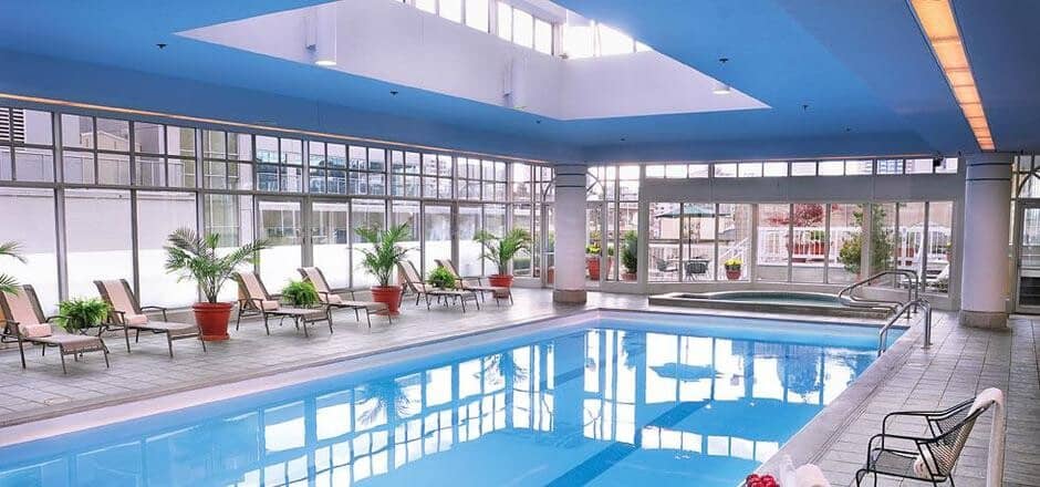 Indoor pool and hot tub with atrium skylight and poolside loungers