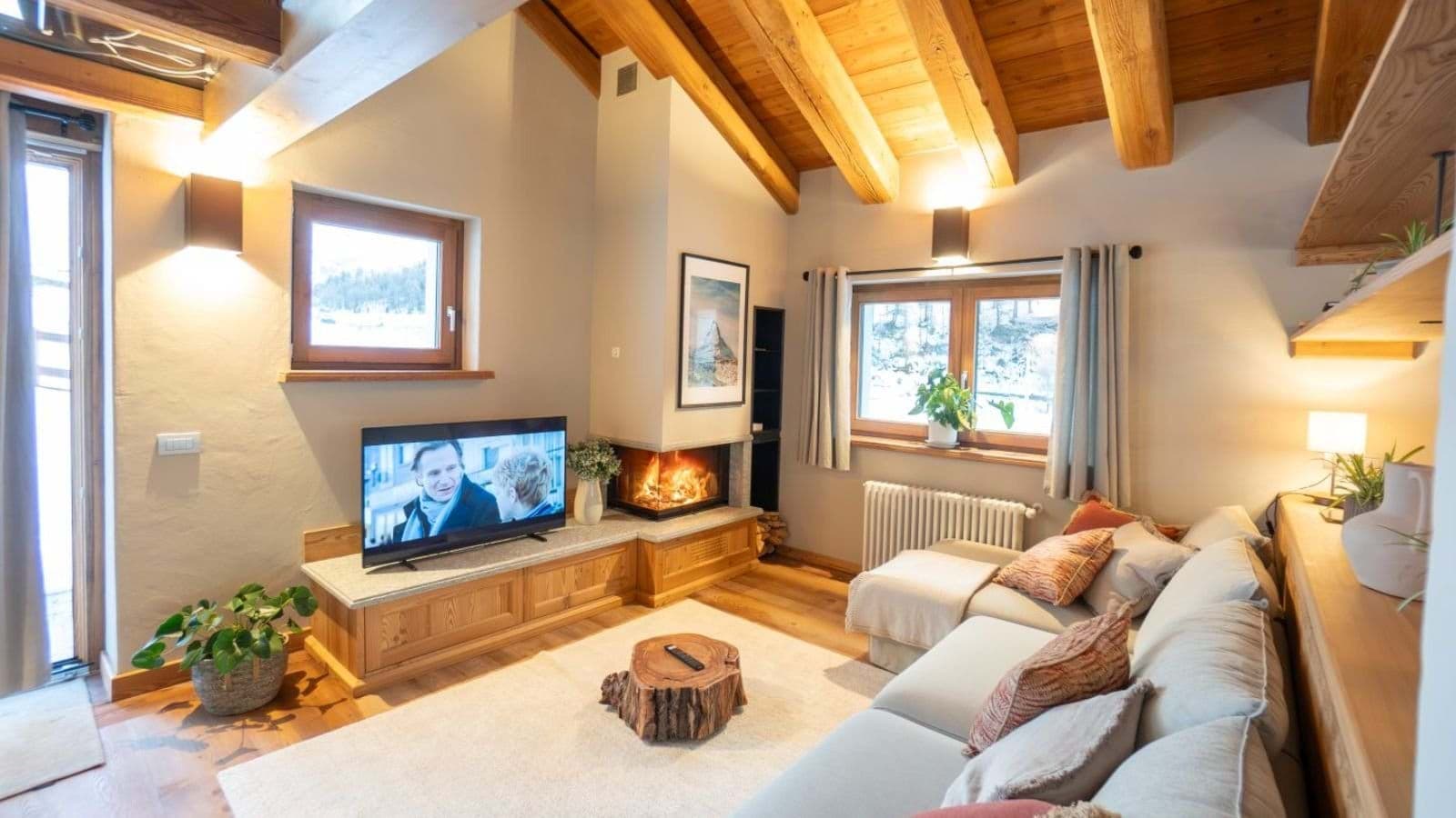 Living area with wood-burning fireplace, sectional seating, and exposed timber beams