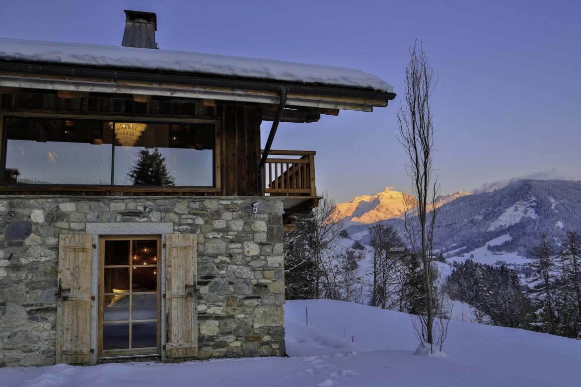 Stone-clad chalet exterior with private balcony and panoramic alpine peak views
