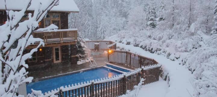 Fenced outdoor pool and hot tub area with winter forest views