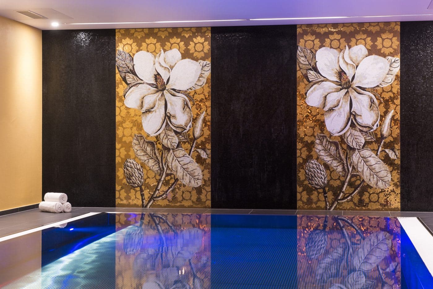Indoor swimming pool with custom floral mosaic mural and poolside towels