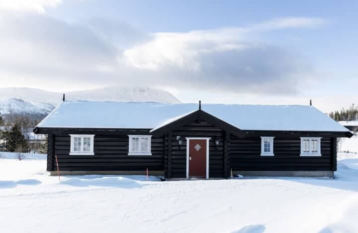 Black timber cabin exterior with snow-covered roof and mountain views