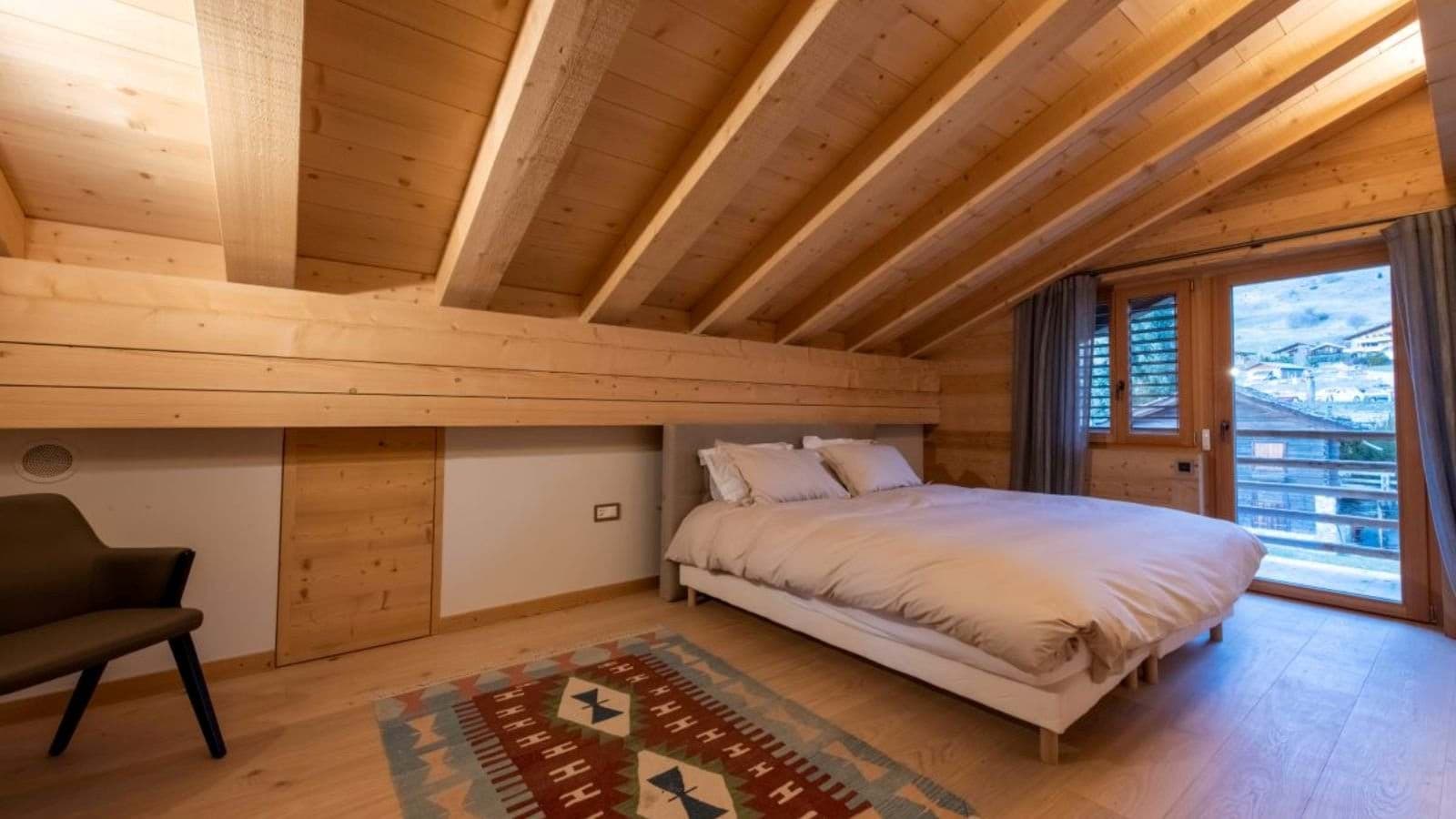Attic bedroom with queen bed, vaulted timber ceilings, and balcony access