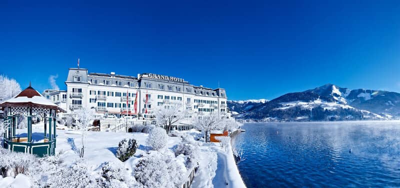 Lakeside hotel exterior with snow-covered grounds and mountain backdrop