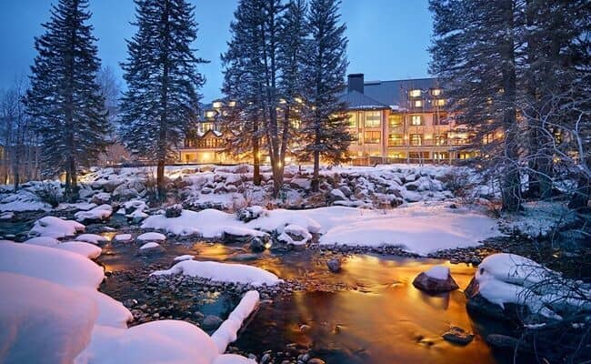 Lodge exterior overlooking snow-covered creek with evening lighting