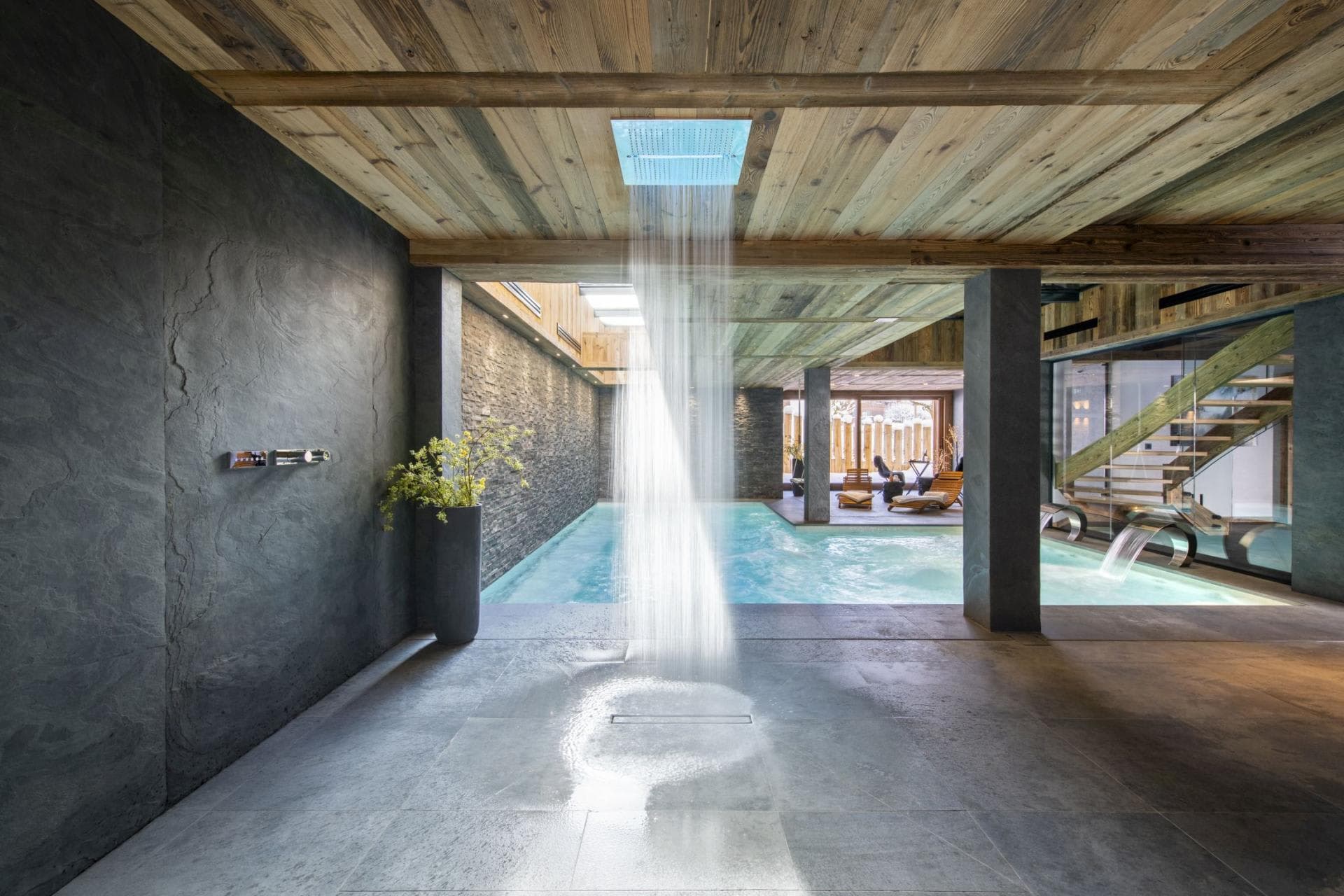Indoor pool area featuring rainfall shower and stone-clad walls
