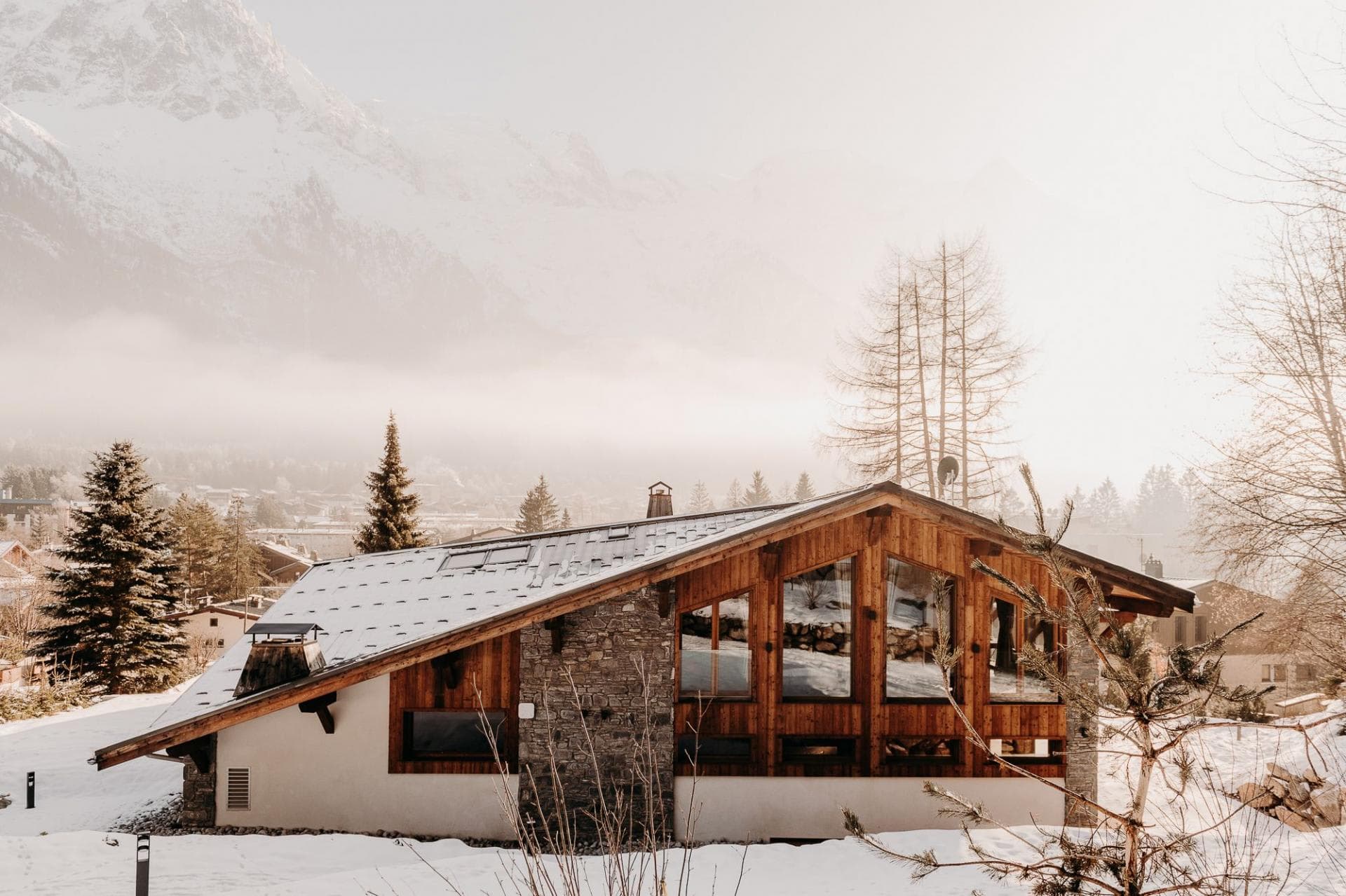 Stone and timber chalet with floor-to-ceiling windows and mountain backdrop