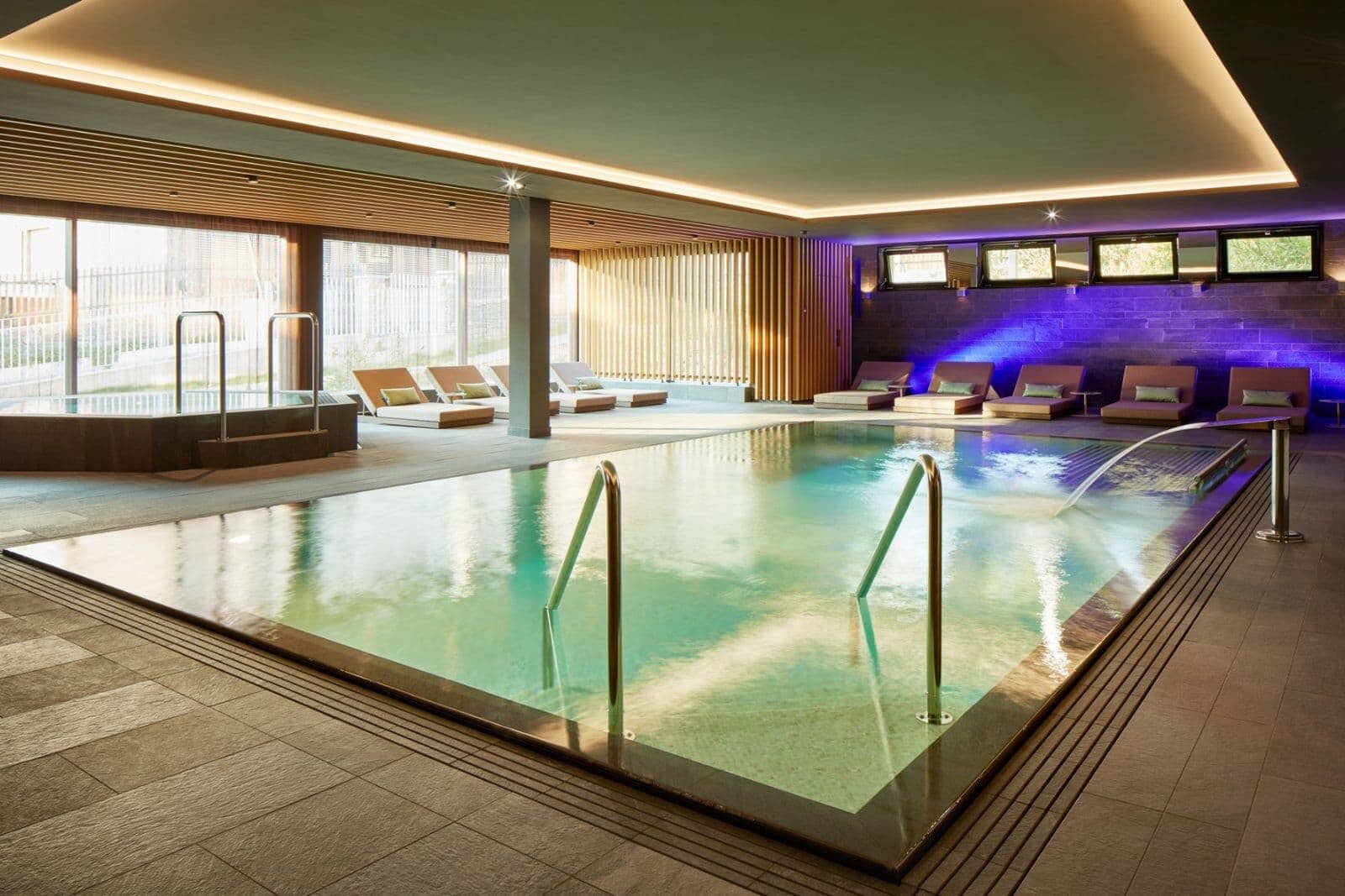 Indoor pool area with water feature, hot tub, and poolside loungers