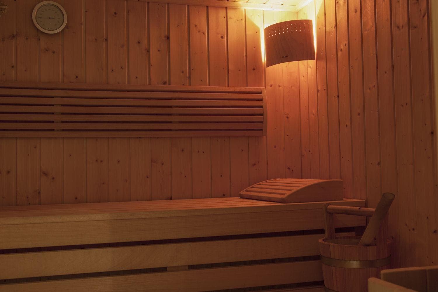 Wood-paneled sauna with bench seating and traditional water bucket