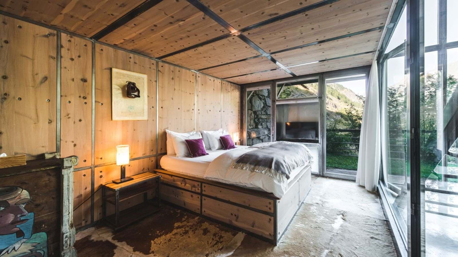 Bedroom with queen bed and floor-to-ceiling windows facing mountain valley