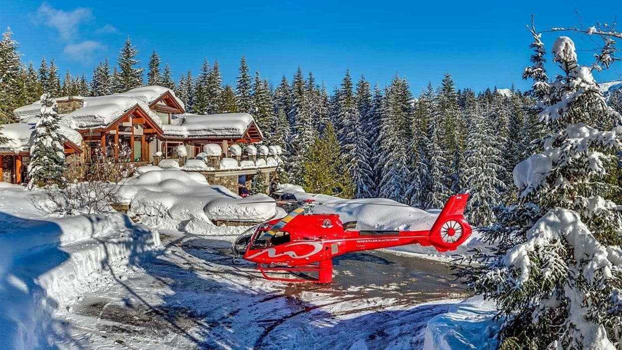 Snow-covered chalet exterior with private helipad and forest setting