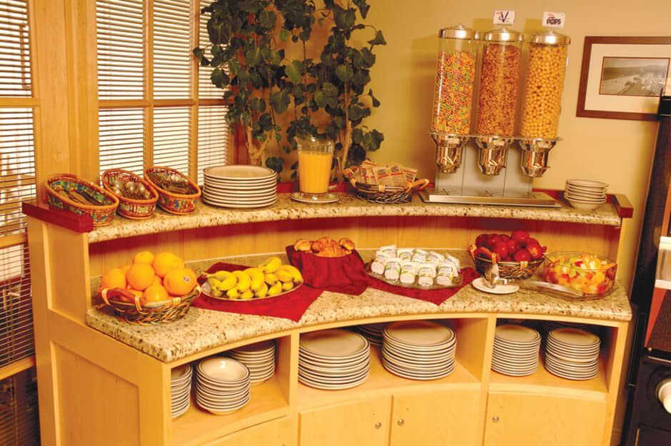 Breakfast buffet station with cereal dispensers, fresh fruit, and pastries