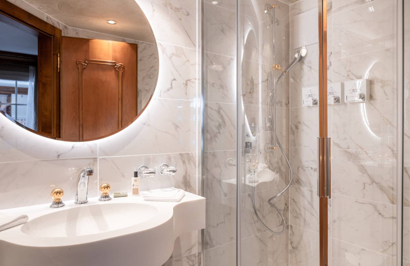 Bathroom featuring marble tile, walk-in shower, and backlit circular mirror