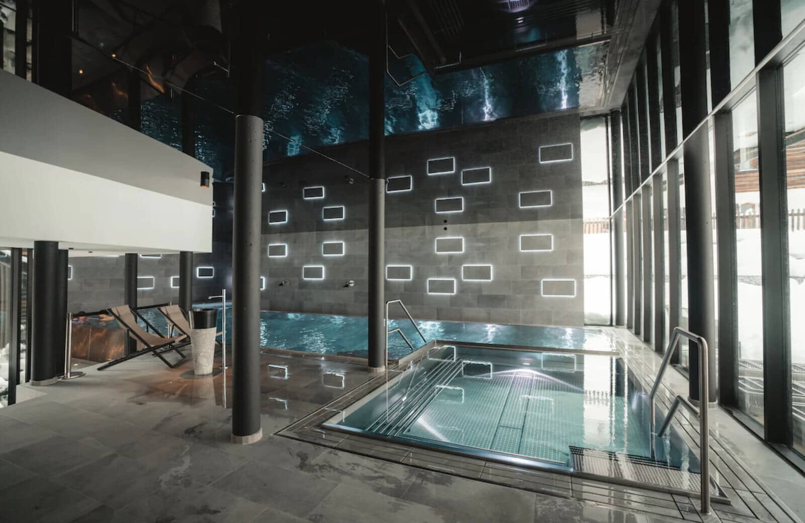 Indoor pool and hot tub with floor-to-ceiling windows and lounge seating