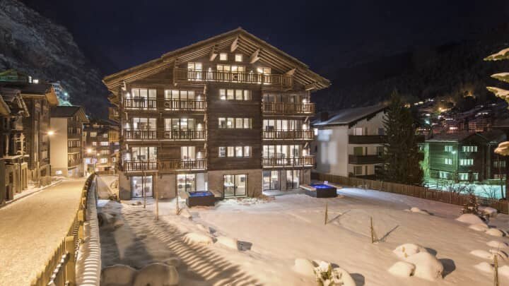 Chalet exterior at night with two outdoor hot tubs and private snow-covered yard