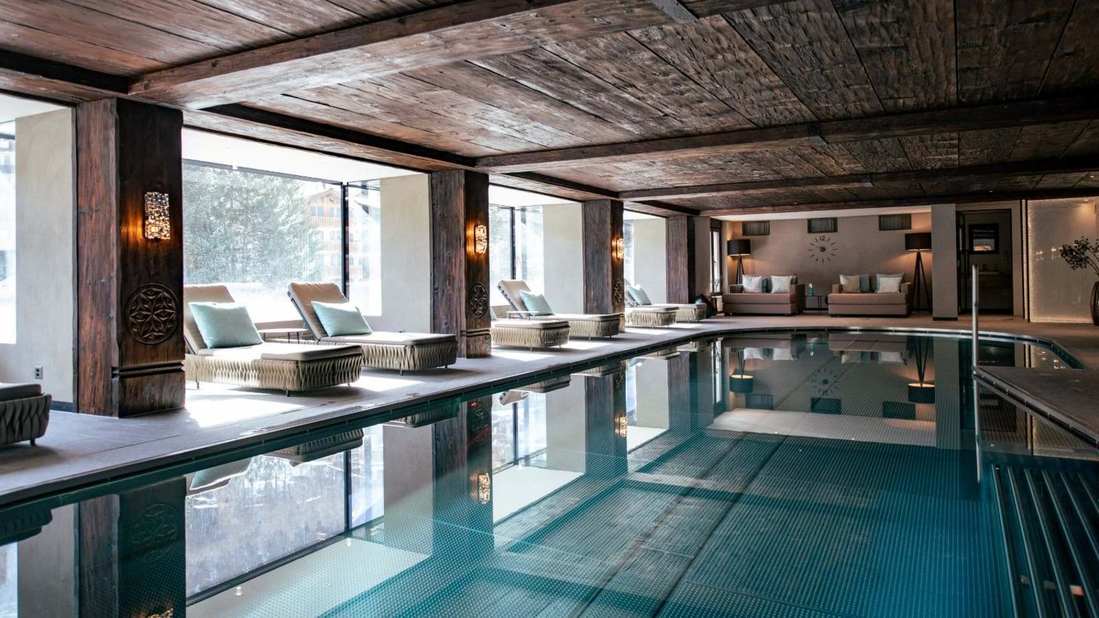 Indoor pool area with floor-to-ceiling windows and poolside lounge seating
