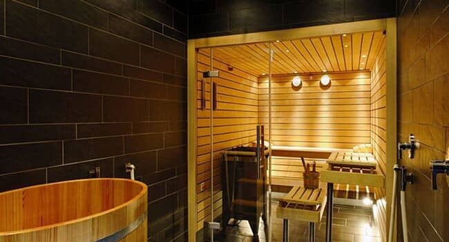 Private sauna with tiered cedar seating and adjacent wooden soaking tub