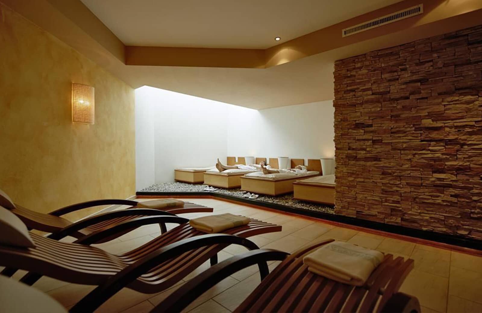 Spa relaxation room with heated loungers and natural stone wall