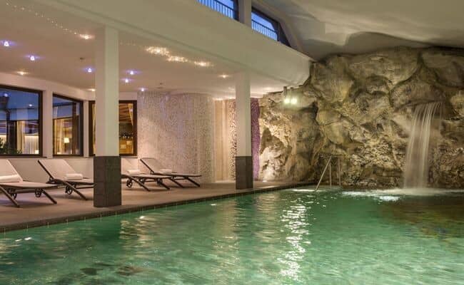 Indoor pool featuring rock wall waterfall and poolside lounge chairs