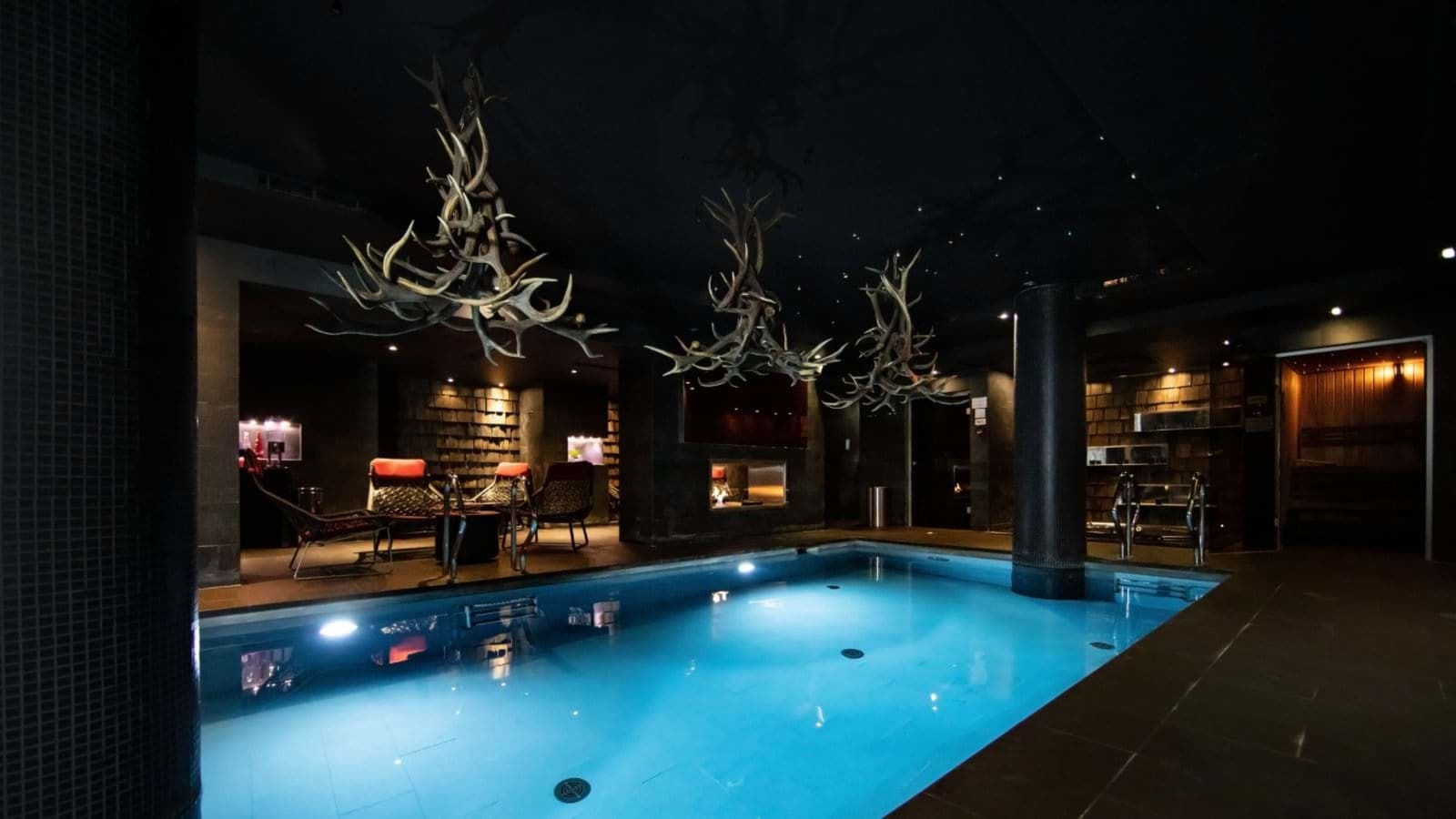 Indoor pool with antler chandeliers, poolside lounge, and private sauna