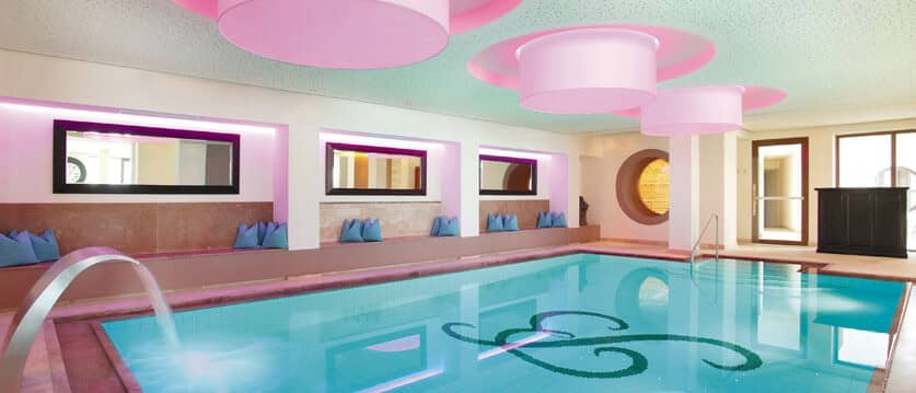 Indoor pool with waterfall feature and poolside bench seating