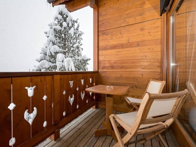 Private wooden balcony with seating for two and snow-covered pine views