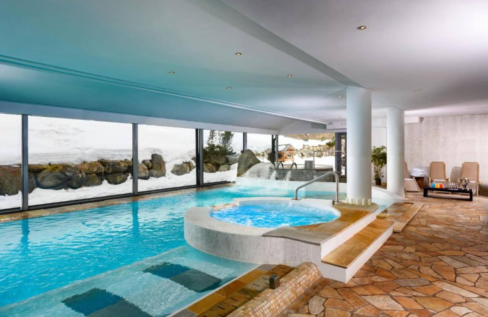 Indoor pool and circular hot tub with floor-to-ceiling snow views