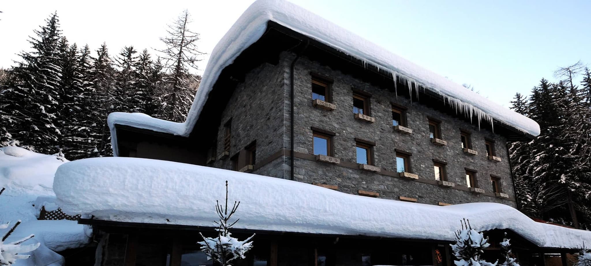 Three-story stone chalet with forest backdrop and heavy snow