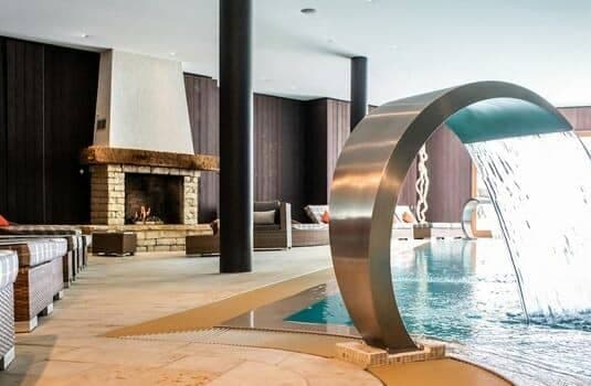Indoor pool with waterfall feature and poolside wood-burning fireplace