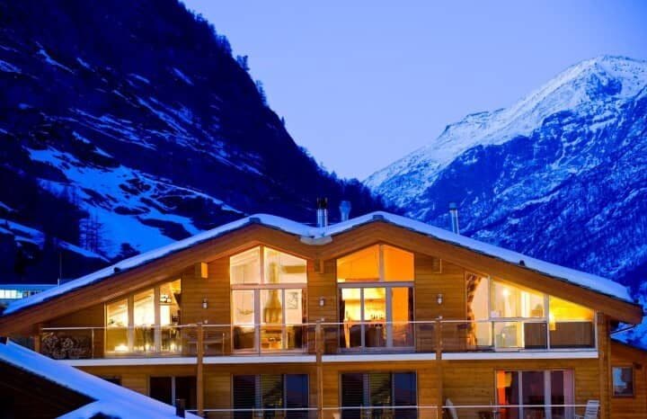 Chalet exterior at dusk with mountain views and wrap-around balcony