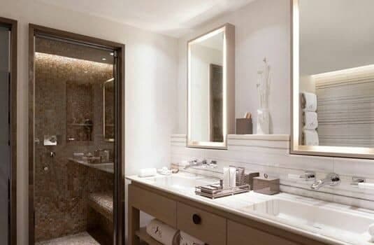Bathroom with dual vanity, backlit mirrors, and walk-in steam shower