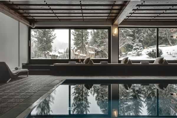 Indoor heated pool with poolside lounge seating and snowy forest views