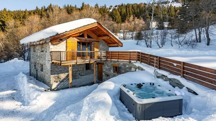Stone chalet exterior featuring private hot tub and upper-level balcony