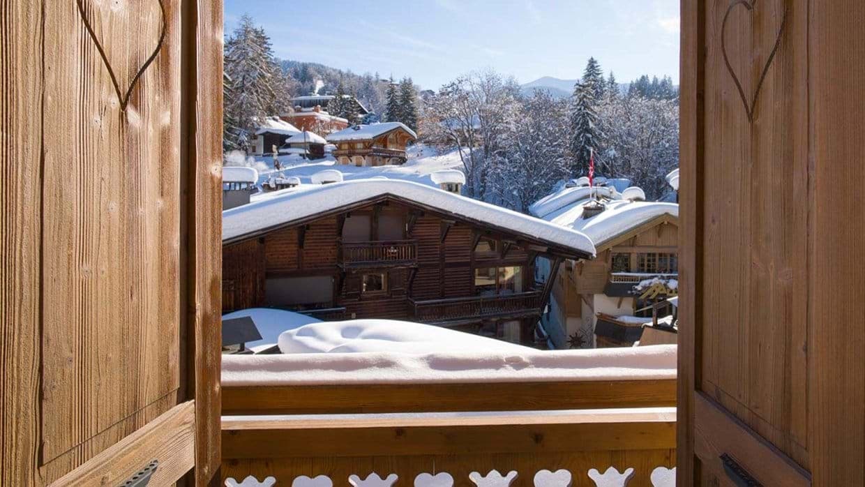 Bedroom balcony view of snow-covered chalets and alpine forest