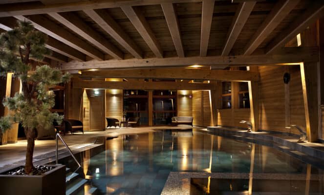 Indoor pool with exposed timber beams and poolside lounge seating