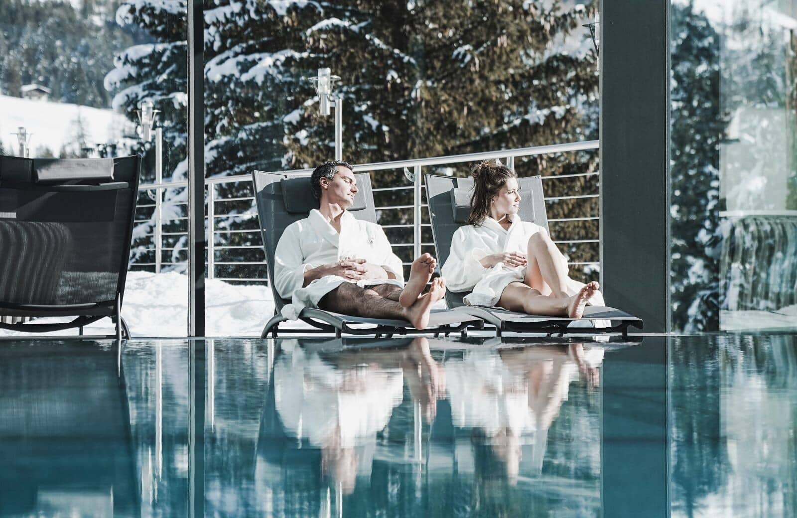 Indoor heated pool with poolside loungers and floor-to-ceiling mountain views