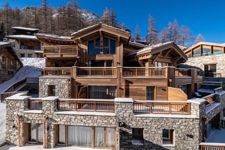Ski chalet exterior with multiple wrap-around stone and timber terraces