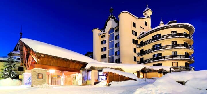 Ski-in/ski-out hotel exterior featuring private balconies and lit snow-covered entrance