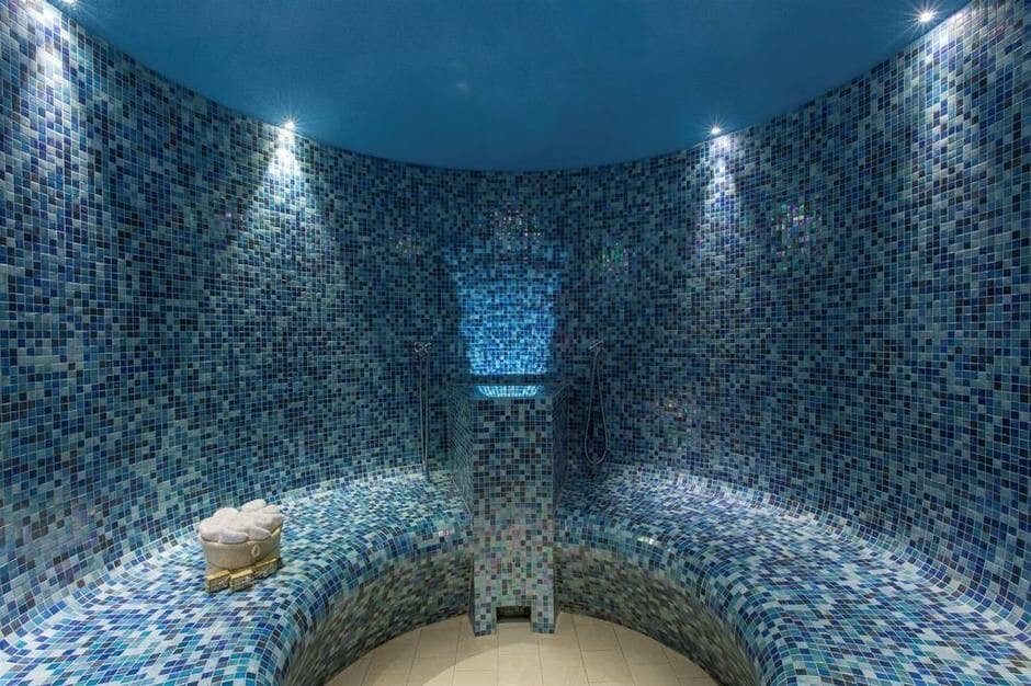 Mosaic-tiled steam room with heated bench seating and dual hand-showers