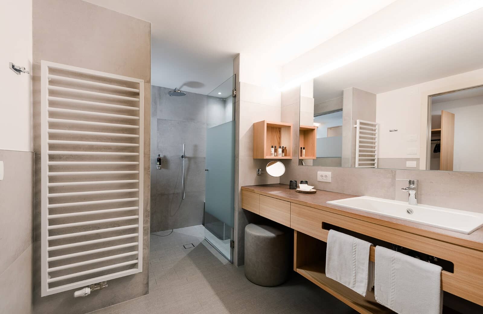 Bathroom featuring heated towel rack, walk-in rainfall shower, and vanity seating